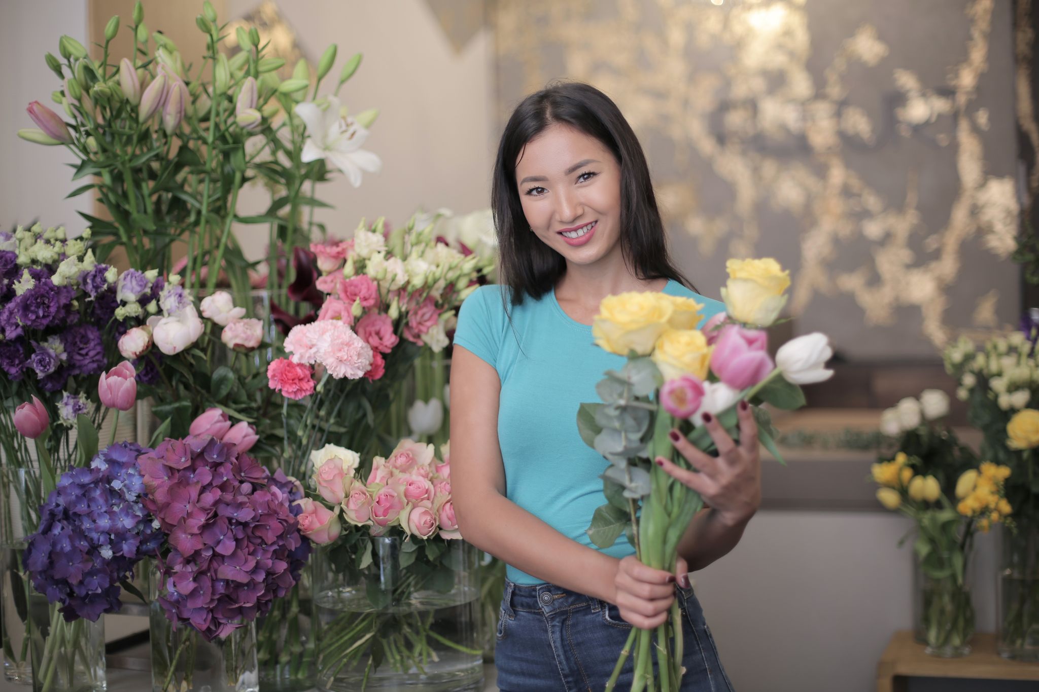 A cheerful woman holding a bouquet in a colorful flower shop.