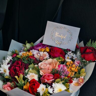 A vibrant bouquet of mixed flowers with a card reading 'Beautiful' against a dark background.