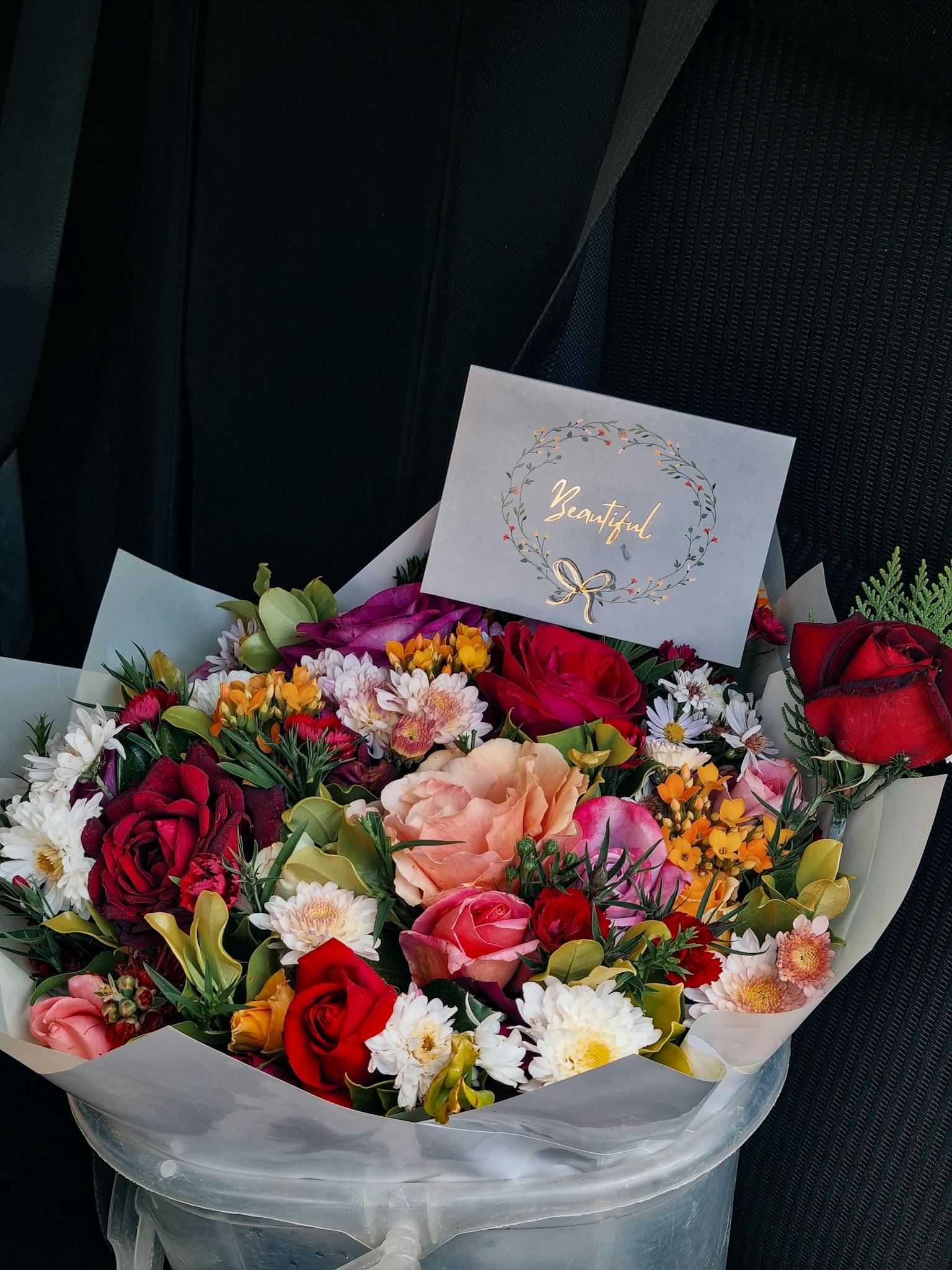 A vibrant bouquet of mixed flowers with a card reading 'Beautiful' against a dark background.