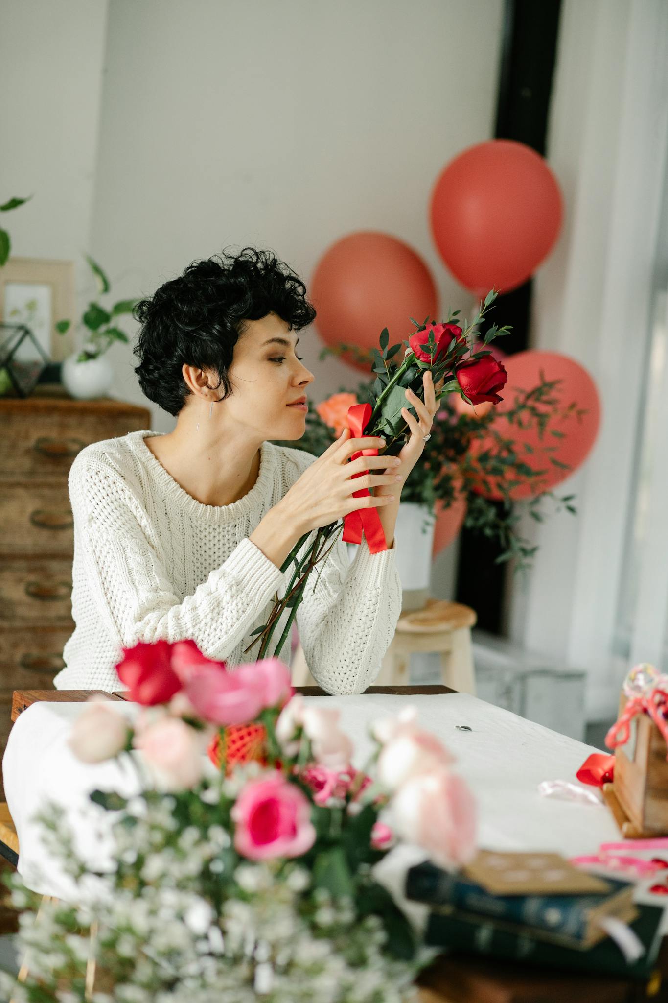 Calm female with tied bouquet of flowers in hands sitting at table while arranging roses during preparation for festive event