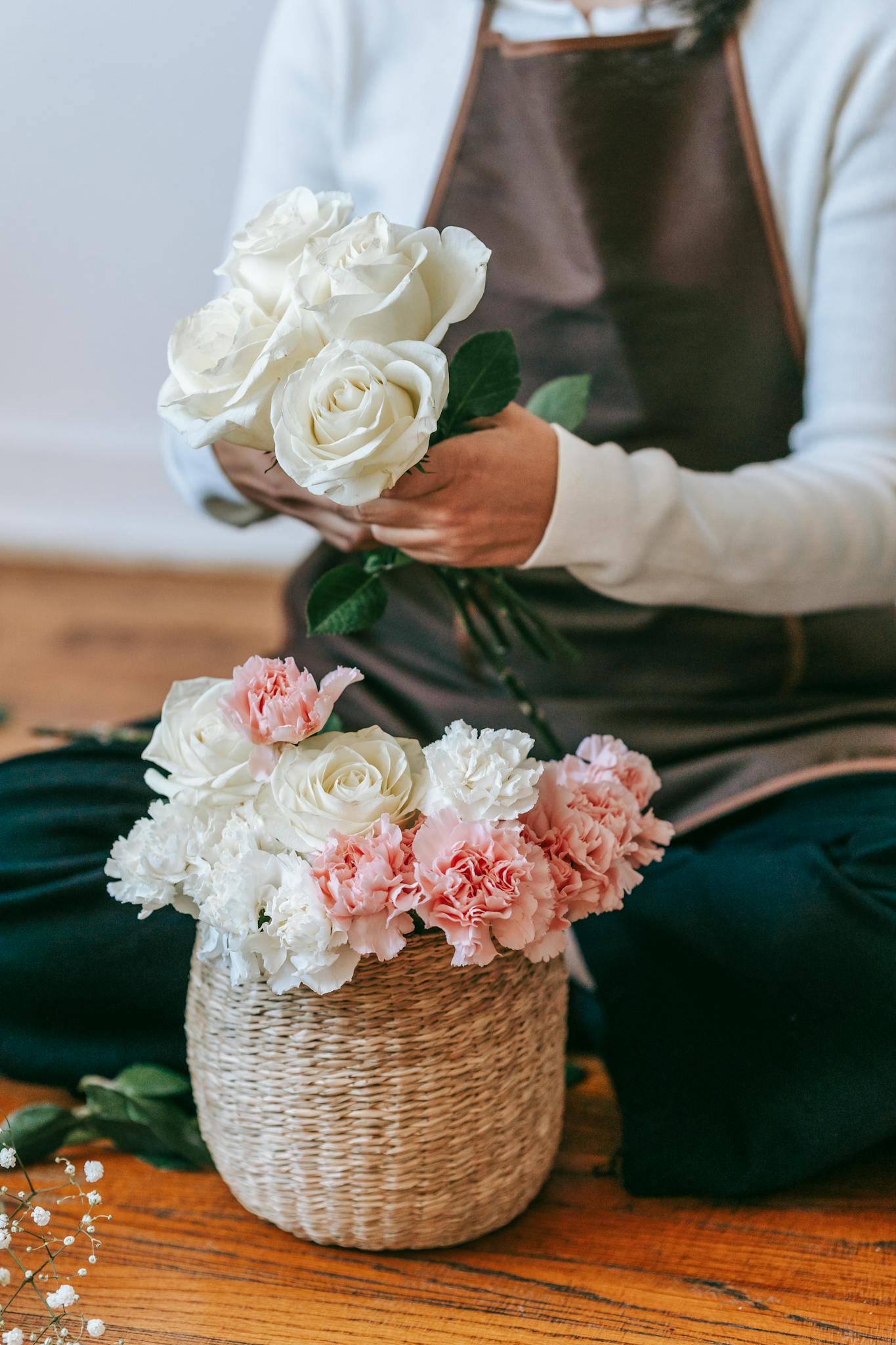 Crop unrecognizable woman florist in apron arranging bouquet with white roses and colorful chrysanthemums in light room