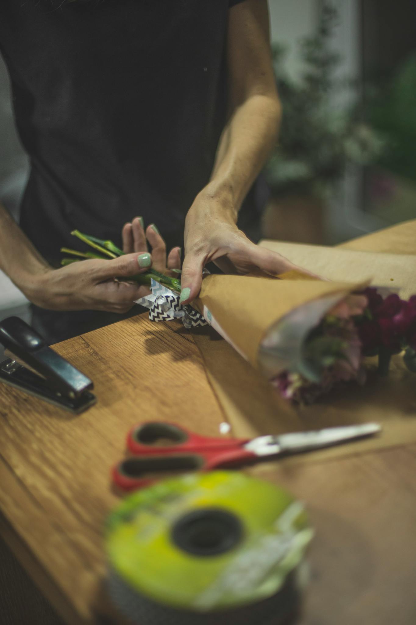 Florist skillfully arranging a vibrant bouquet with tools on a wooden table.